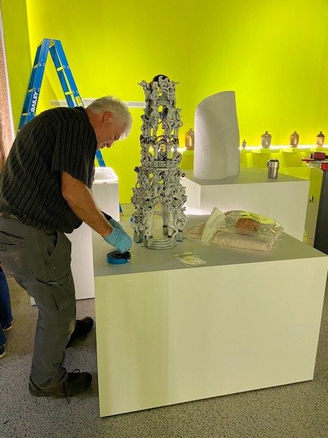 Conservator Tim Morris is finalising object supports for ceramics on open display plinths in gallery space. Ceramicist Brian Doar's 'Welcome to the Herb Alpert Pleasure Dome' artwork is in the foreground.